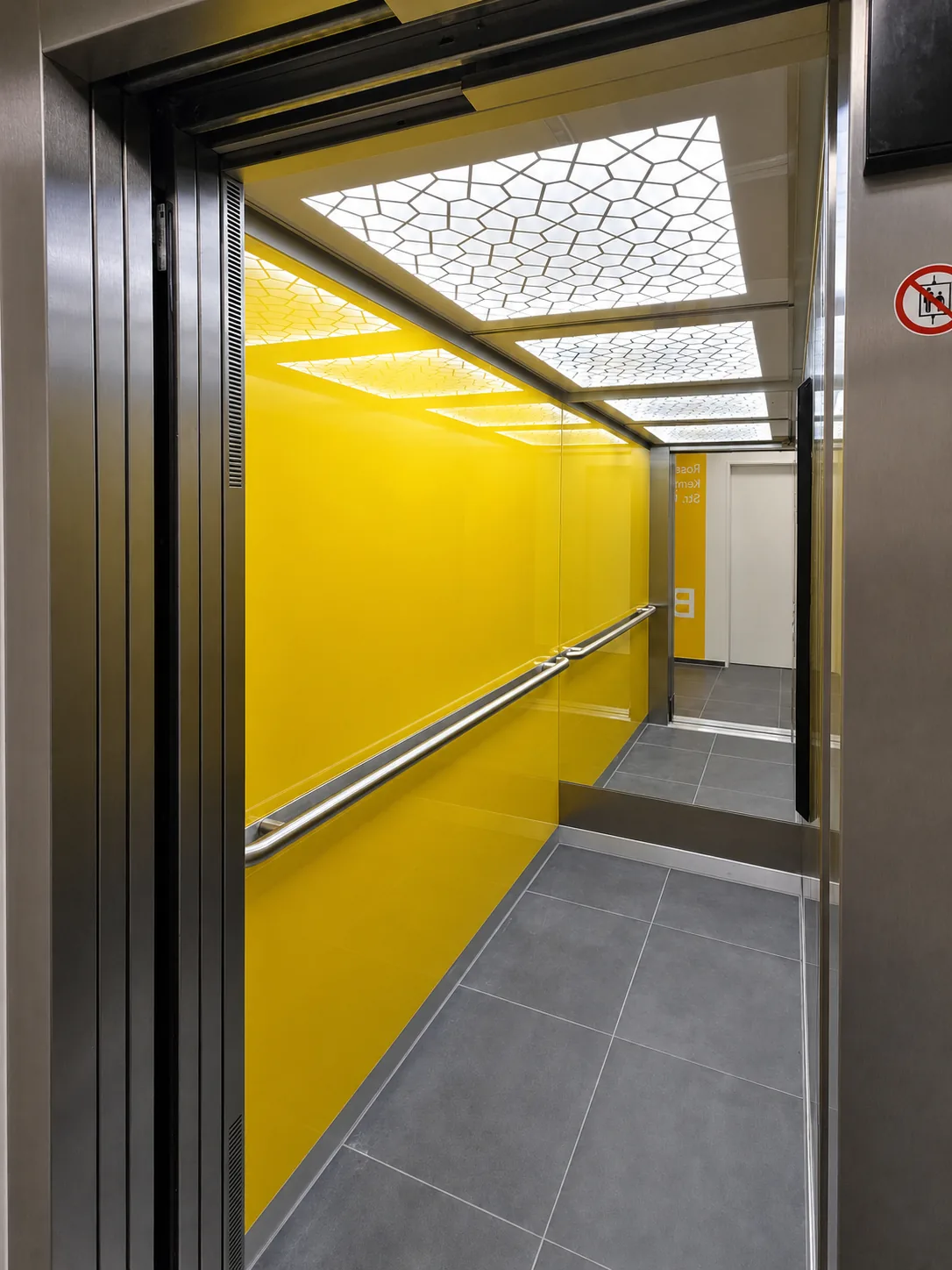 Aufzugskabine mit gelber Glasauskleidung und Lichtdecke