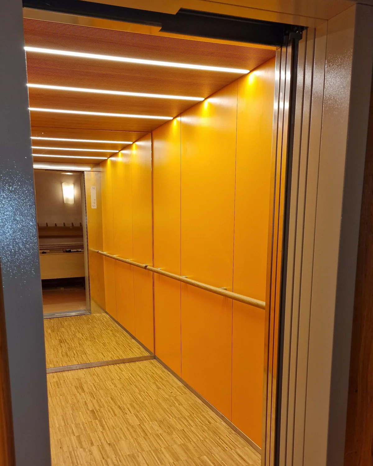 Elevator cabin with a bespoke slatted ceiling and warm wall finishes